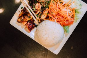 Top view of an appetizing Asian dish with rice, grilled chicken, and fresh vegetables.