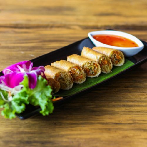 Crispy Thai spring rolls served with a sweet chili sauce, garnished with fresh greens.