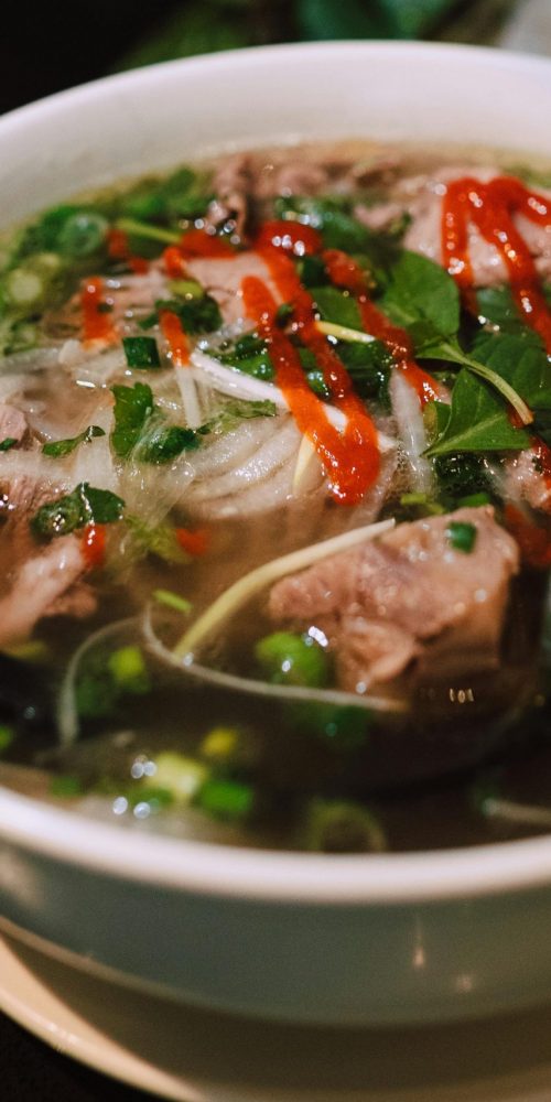 Delicious bowl of traditional Vietnamese pho garnished with fresh herbs and spicy sauce.